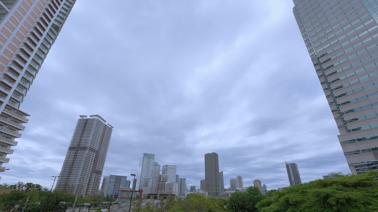 A low-angle shot of a Tokyo cityscape with tall modern skyscrapers and residential buildings against an overcast sky