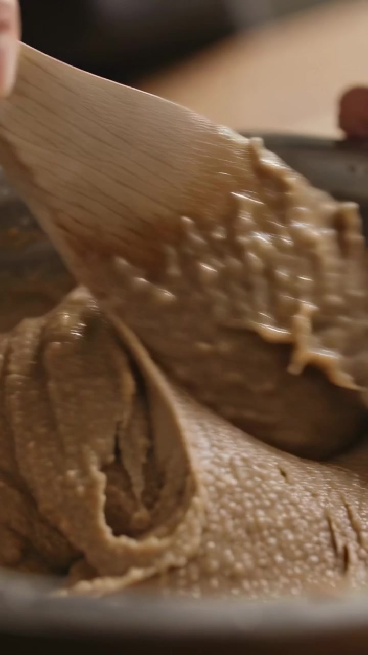 Vertical video: Pulling wooden spatula, hand folding and leveling batter in metal bowl at home