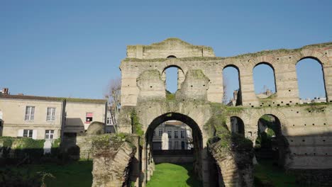 Roman-Amphitheatre-ruins-in-Bordeaux-France-with-remaining-stone-arches-near-residential-areas,-Aerial-pan-left-shot