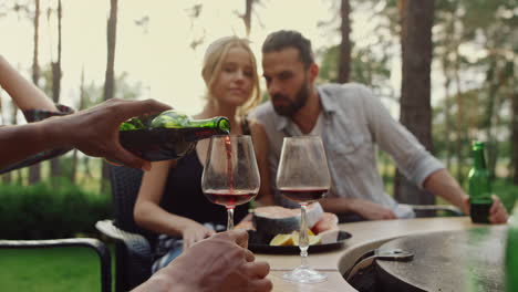 unknown guy pouring wine in glasses on backyard. couple relaxing in forest