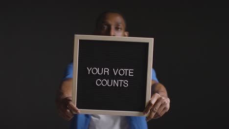 Portrait-Of-Man-Holding-Your-Vote-Counts-Sign-In-Election-Against-Black-Background