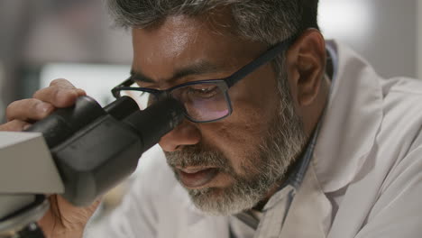 focused senior scientist examining sample under microscope in lab