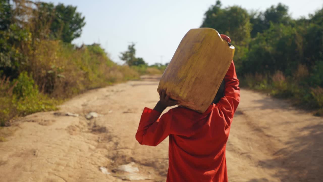 Slowmotion shot of African kid carrying water bottle on his head after fetching water from the river