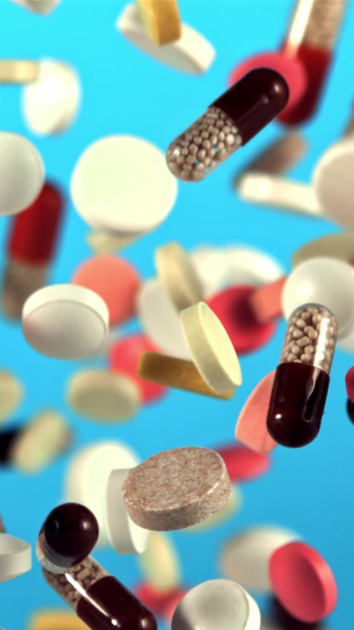 Various Pills and Capsules Falling in Slow Motion Against a Blue Background