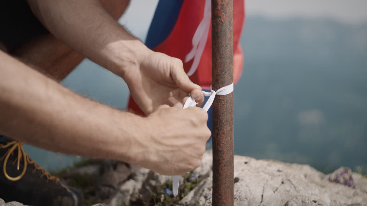 hombre atando la bandera eslovena al poste para dejar que fluya en la cima de la montaña