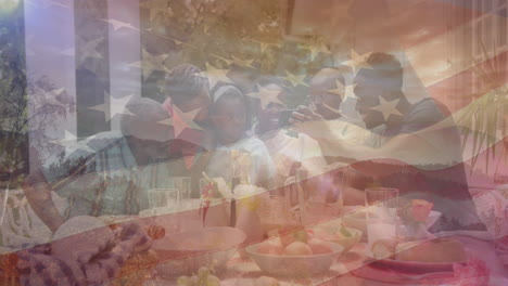 animación de la bandera de los estados unidos de américa sobre una familia afroamericana cenando en el jardín