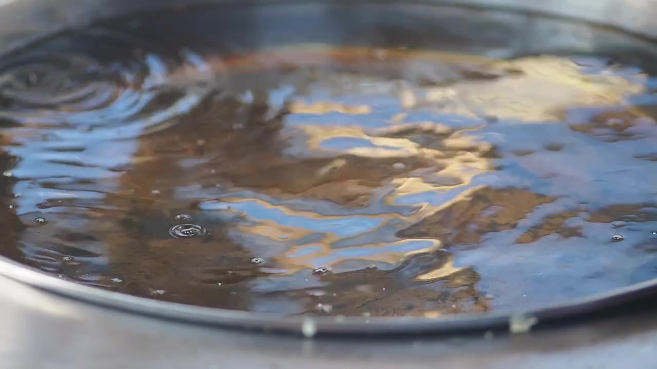 Gocce d'acqua che cadono e creano increspature in una padella di metallo