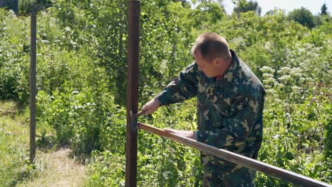 builder taps on fence carcass with hammer against weeds