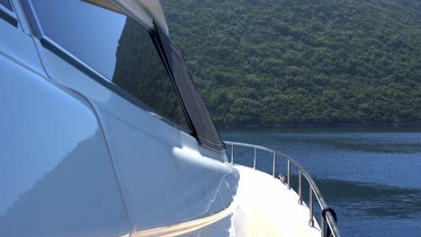 detail of yacht at sea with green forested mountain coastline