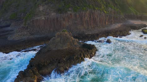 Brechende-Wellen-Auf-Basaltseestapeln-Mit-Touristen,-Die-Auf-Sandsteinklippen-An-Den-Kathedralenfelsen-In-Kiama,-New-South-Wales,-Australien,-Spazieren-Gehen