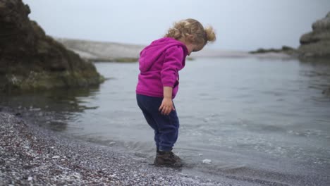 Playful-Blond-Girl-Kid-On-Sandy-Beachfront-With-Calm-Ocean-Water