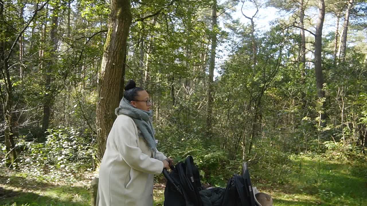 Fast walking young mother with twin baby stroller in the autumn forest.