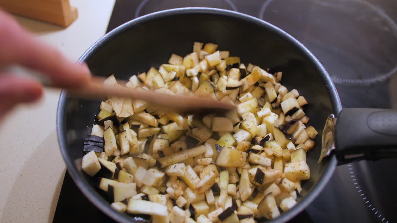 Close up view of sliced eggplant been stirred on a frying pan while been cooked