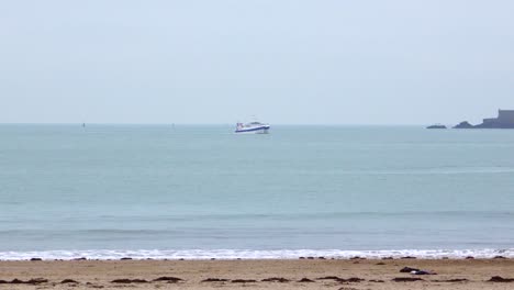 a slow-motion shot facing the open sea off dinard. at the center of the frame, a small motorboat crosses the horizon under a grey winter sky, evoking calm and solitude.
