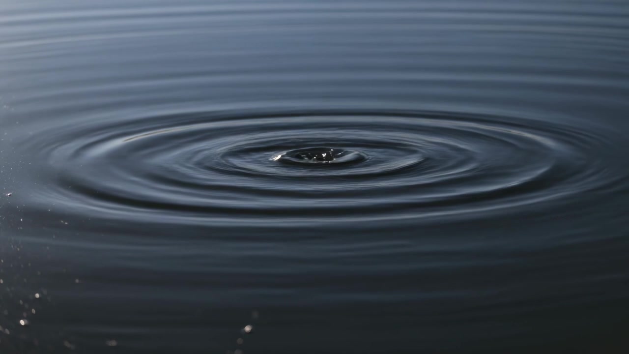 Mostrando una goccia centrale che impatta acqua calma e scura, creando increspature rotonde che si diffondono e smorzano l'energia.