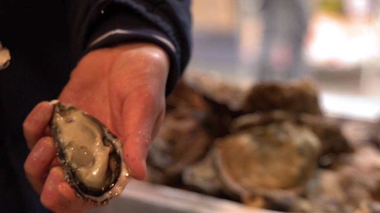 A street food worker uses a knife to shuck a fresh oyster at Tsukiji Market