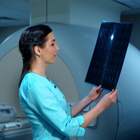 side view of female specialist with radiography. specialist holds x-ray photo in arms and carefully researches it. woman expert dressed in medical coat.