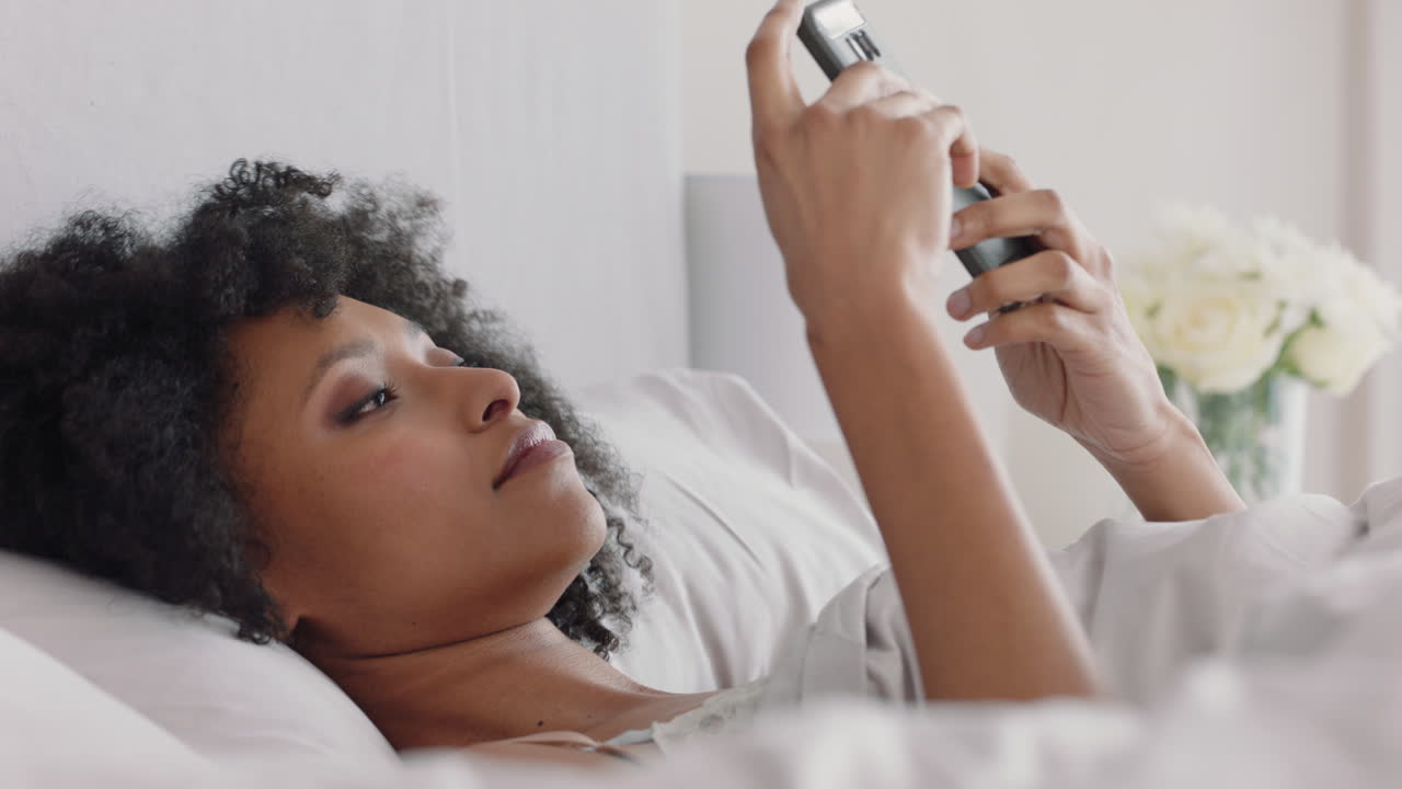 bella donna che usa lo smartphone che manda messaggi a letto che naviga i messaggi dei social media che si gode la condivisione di un weekend rilassante a casa