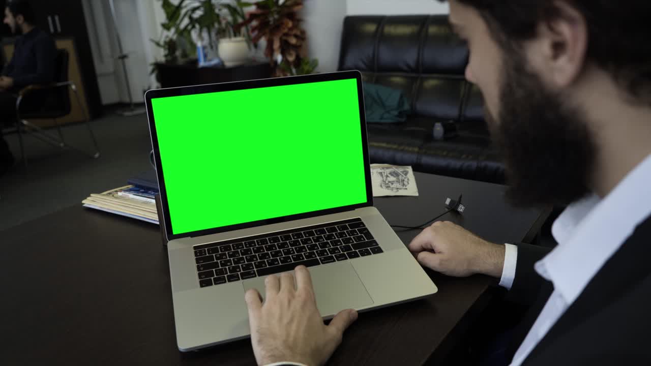 hombre trabajando en una computadora portátil con una pantalla verde en una oficina