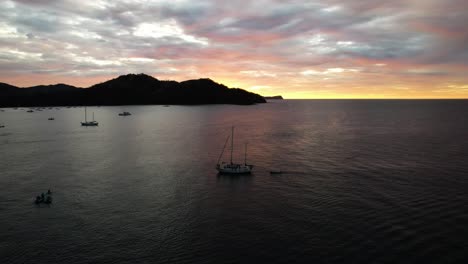 drone rotating around sailboat navigating at colourful sunset in pacific ocean seashore, costa rica