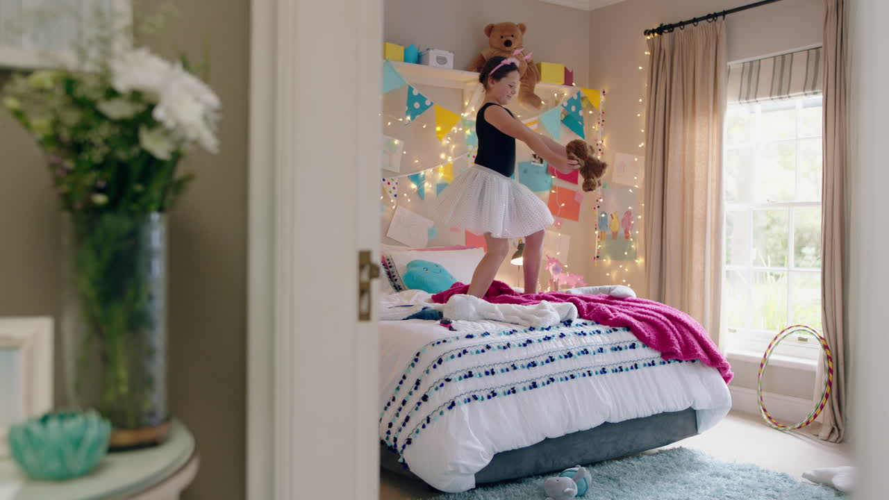glückliches teenager-mädchen tanzt auf dem bett, trägt eine ballett-tutu, hat spaß und tanzt mit einem teddybären im schlafzimmer