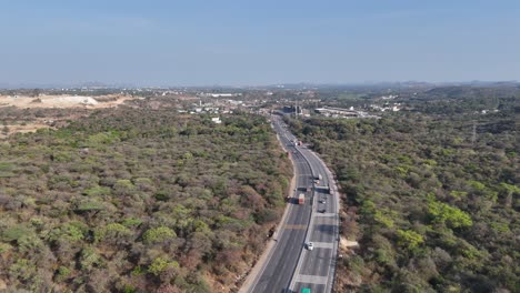 aerial view of a multi-lane highway winding through a vast, dry forested landscape. traffic moves towards distant signs of human development, showcasing infrastructure connecting nature and towns