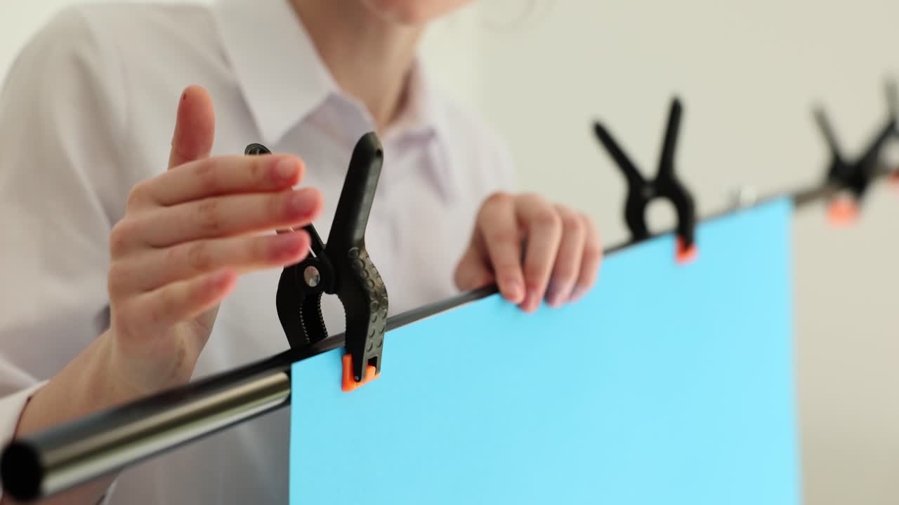 Person setting up a blue backdrop with clamps