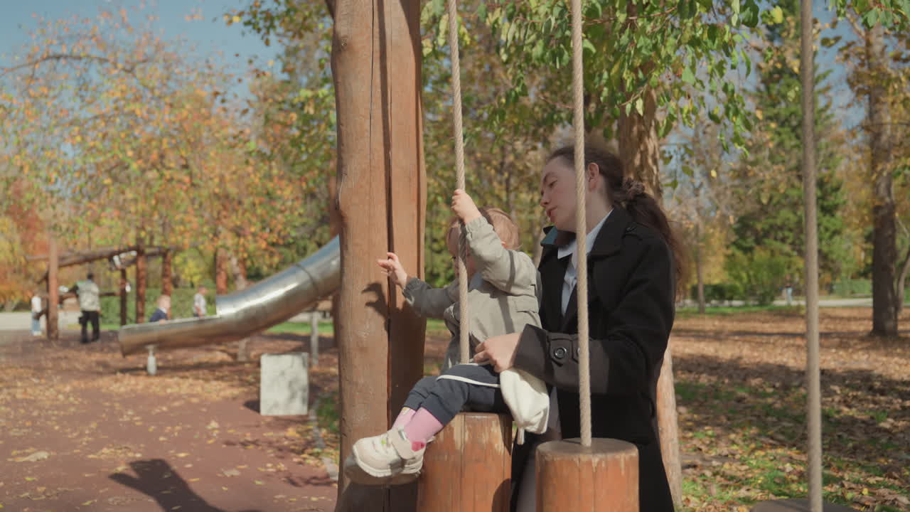 Niño y madre disfrutando de un juego suave al aire libre. Escena serena de madre e hijo compartiendo afecto en exteriores. Entorno de parque tranquilo con madre y pequeño compartiendo gestos tiernos en otoño