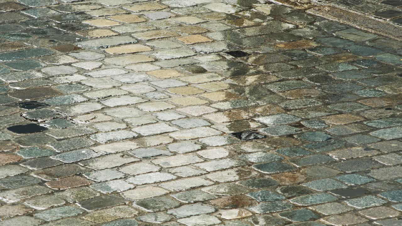 High-angle close-up captures raindrops splashing across historic cobblestone pavement