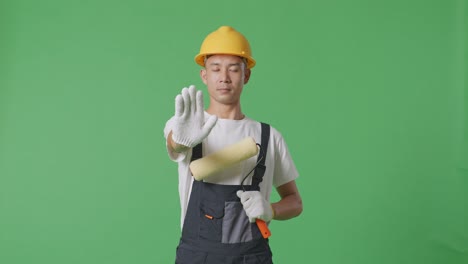 Asian Man Painter Wearing Safety Helmet Looking At Camera And Disapproving With No Hand Sign While Standing In The Green Screen Background Studio