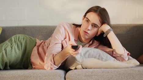 caucasian non-binary transgender woman lying on sofa, watching tv