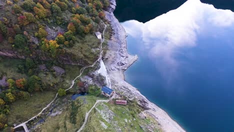 dam keeper chalet at lac d'oô artificial lake in the french pyrenees with small water stream flowing from the dam wall, aerial top view orbit around shot