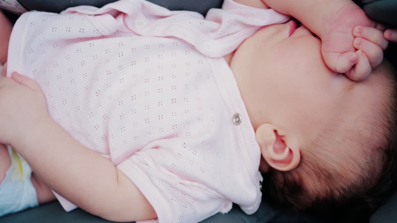 Close up of a baby wearing a pink outfit, peacefully sleeping with a hand near the face