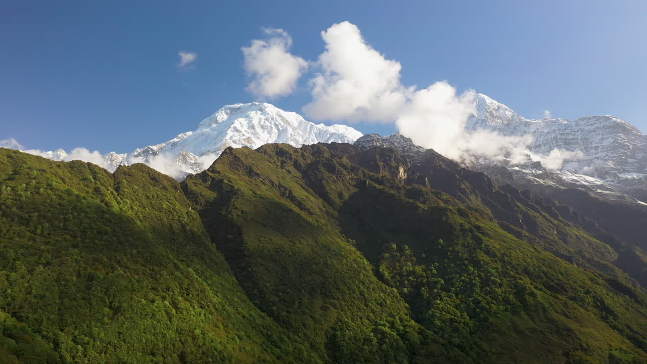 네팔 안나푸르나 산맥의 산면과 눈 덮인 봉우리에 빛나는 태양의 장대한 공중 드론 샷