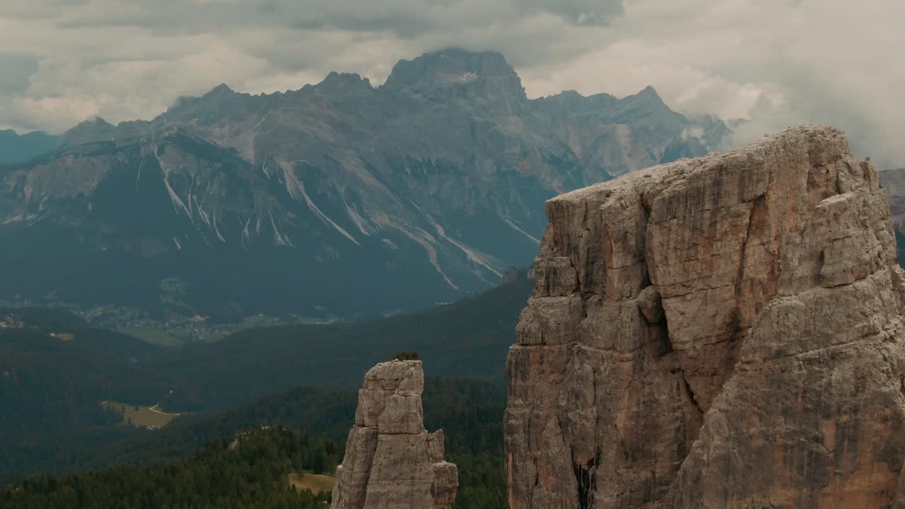 vista aérea volando más allá de rocas masivas a altas montañas en el fondo, bosque verde en la parte inferior, día nublado, grado de color cinematográfico