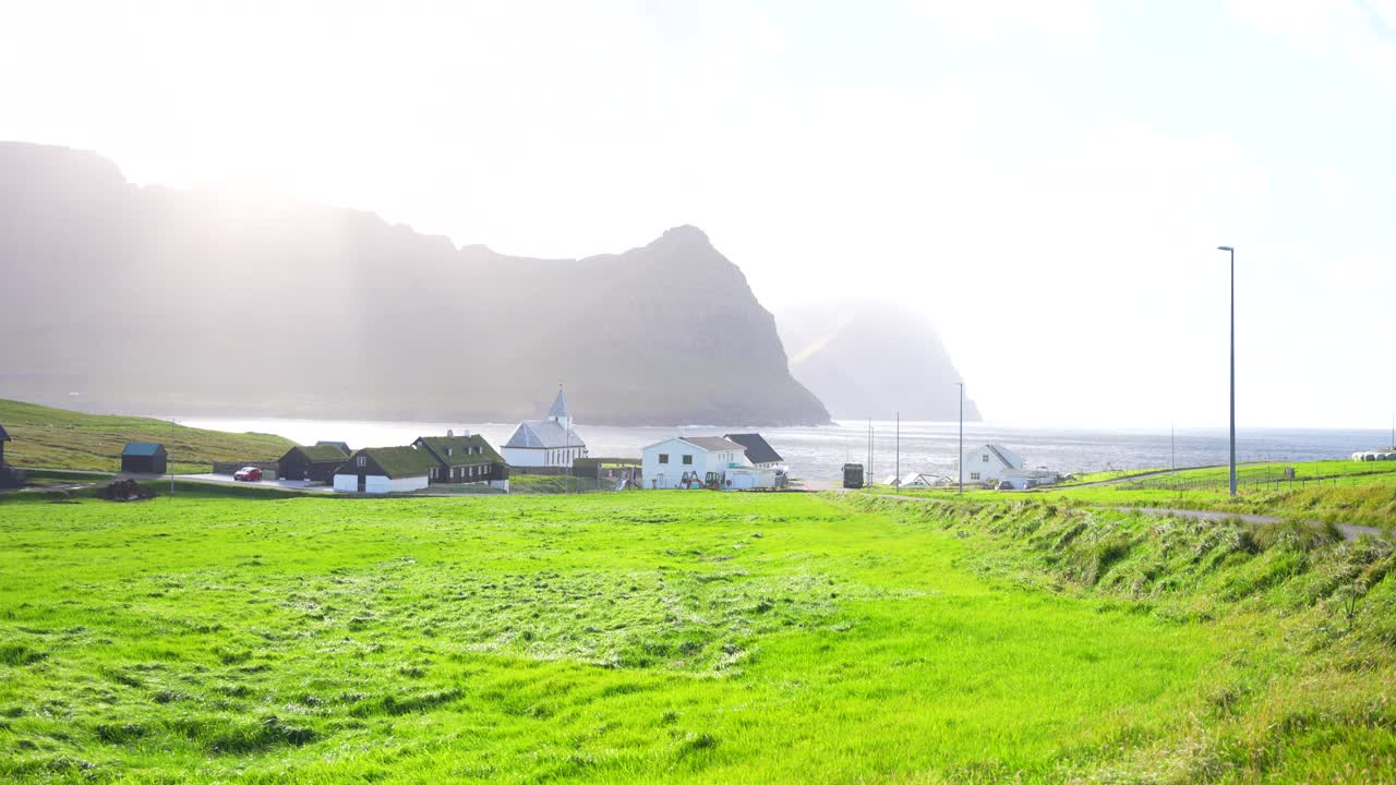 Clouds opening after the storm let sunlight through over Vidareidi's turf roof houses, Faroe Islands