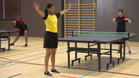 playing table tennis, woman in yellow shirt warming up in school gym