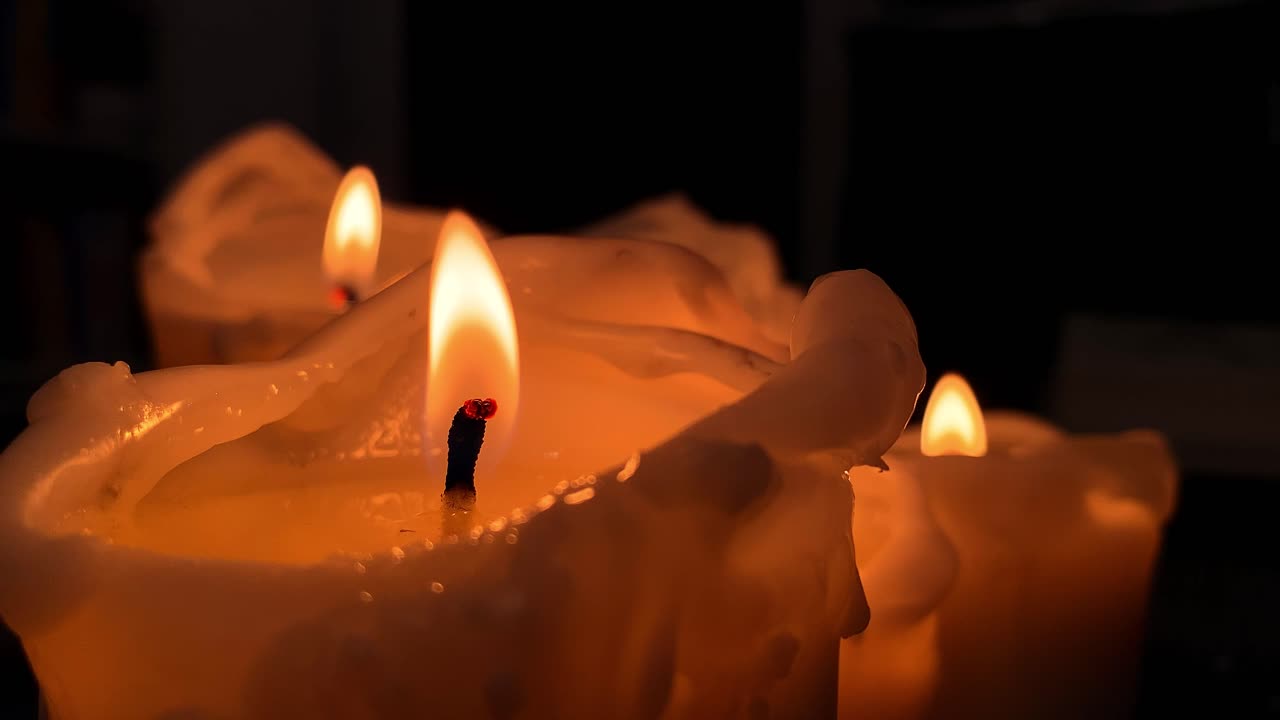 Primo piano di candela arancione accesa su composizione su sfondo nero, fiamma a rallentatore sulla candela.