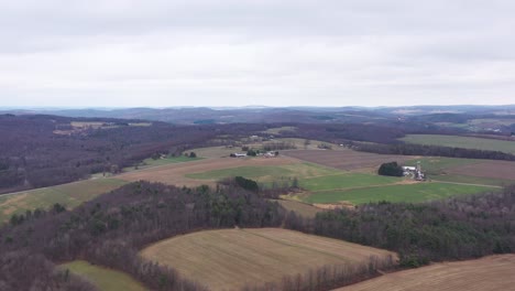 Aerial-Shot-Flying-Over-A-Lush-green-and-brown-Country-Farm-Landscape-On-A-Gloomy-sky