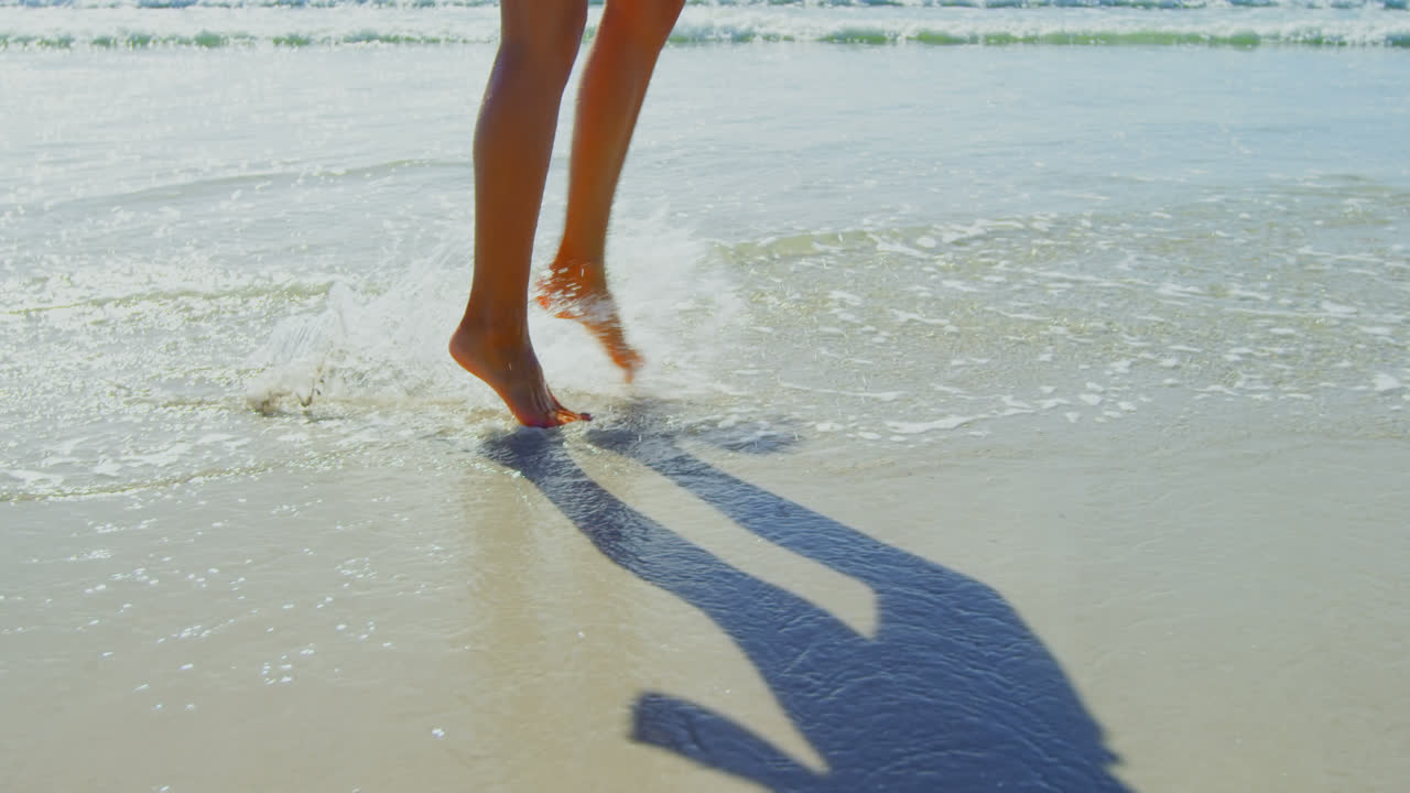 sección baja de la mujer salpicando agua en la playa mientras camina en la playa 4k