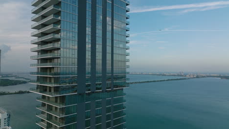 Orbit-shot-around-modern-high-rise-apartment-buildings-with-glossy-facade.-Tall-residential-tower-on-waterfront-at-twilight.-Miami,-USA