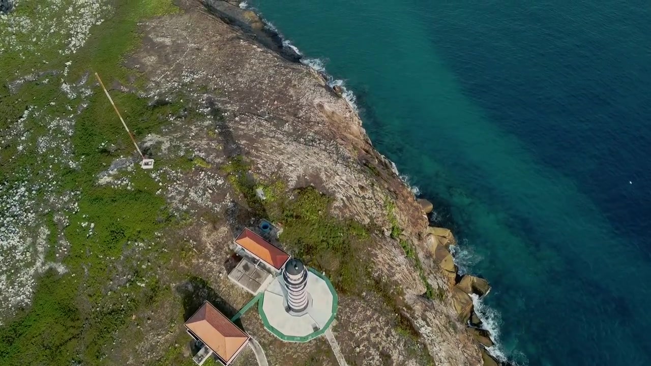 Faro di Farol de Abrolhos sull'isola di Santa Bárbara nel Parco Nazionale Marino di Abrolhos, Caravelas, Bahia, Brasile, sopra la costa rocciosa e le limpide acque atlantiche, ripresa in volo dall'alto in avanti.