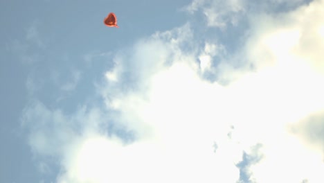 a red heart-shaped balloon floats alone in the sky during sunset