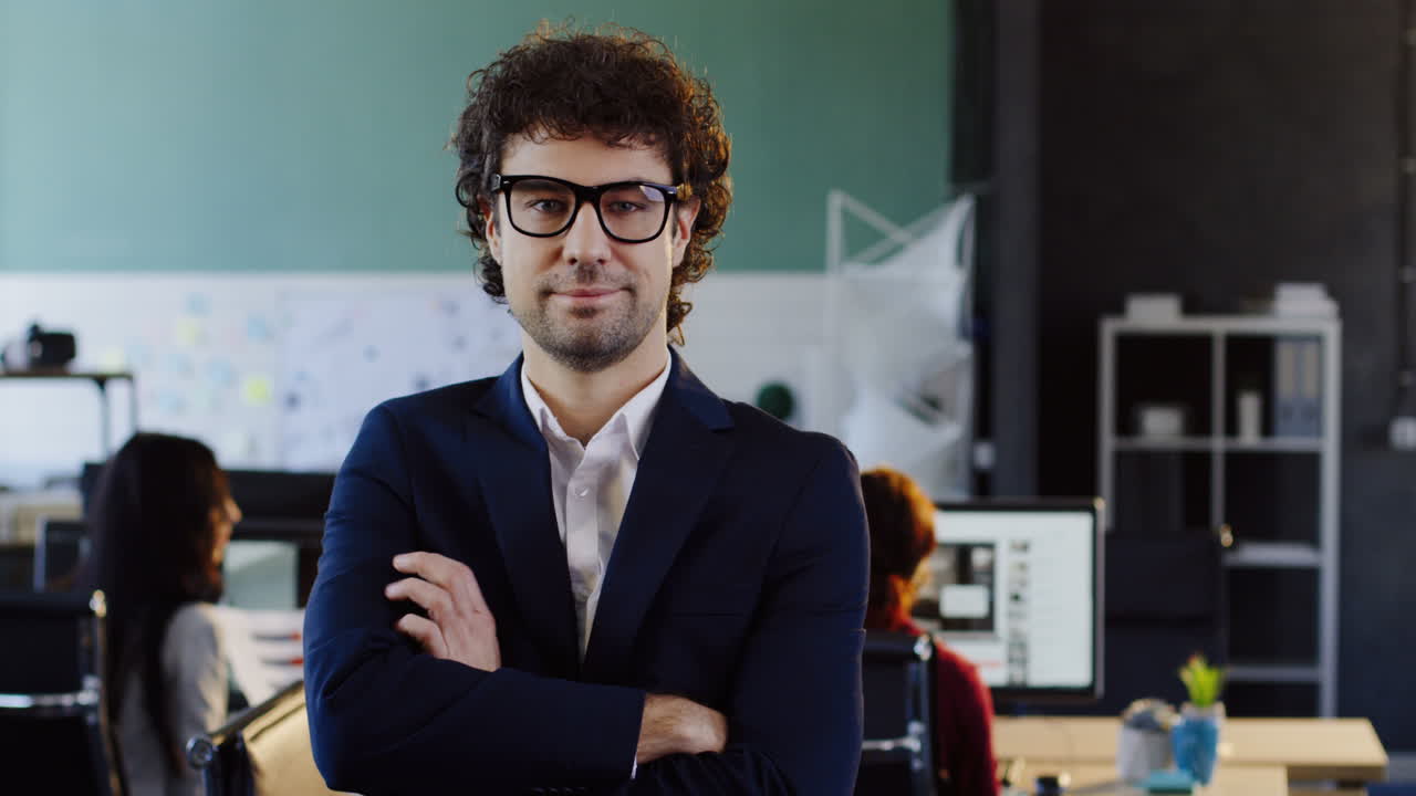 hombre de negocios caucásico con gafas mirando a la cámara con los brazos cruzados en la oficina