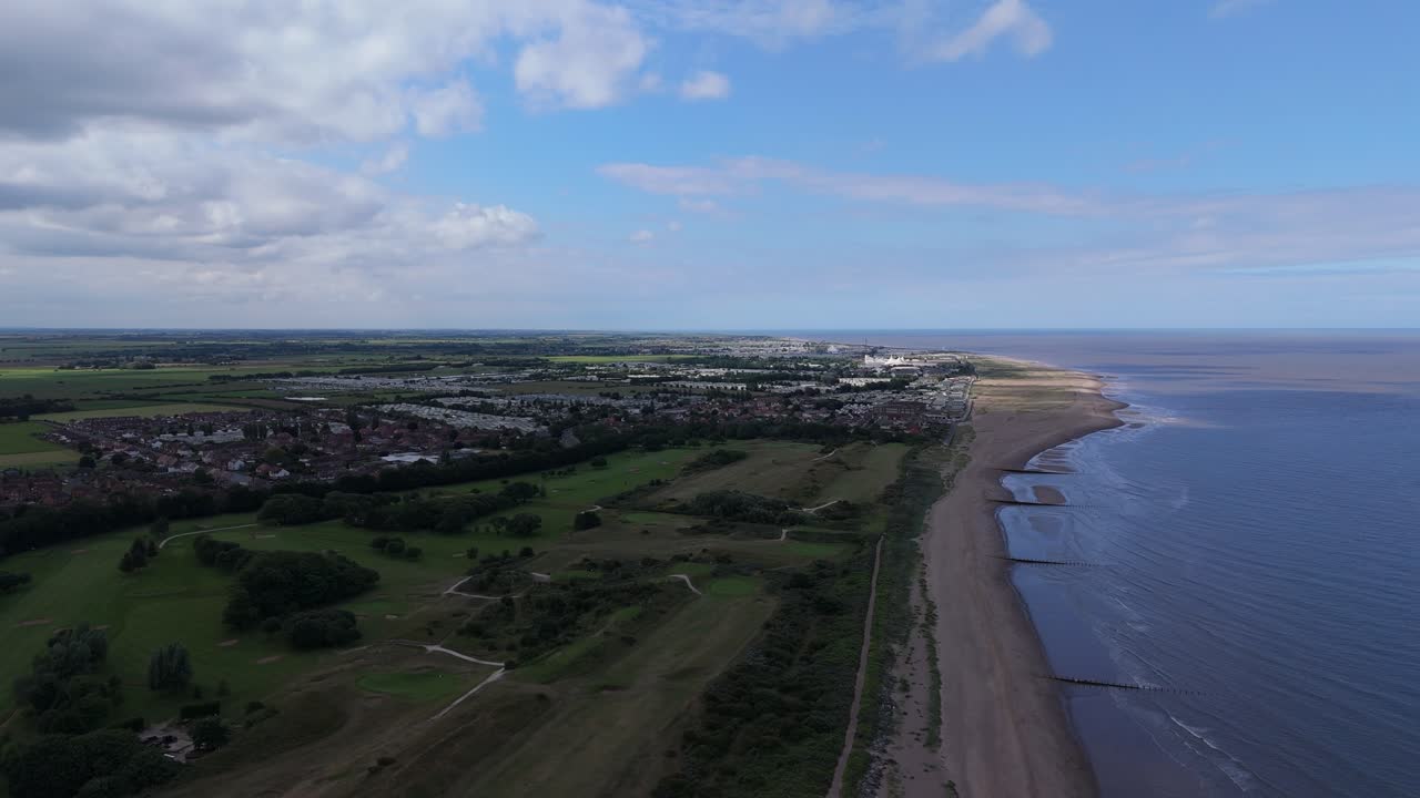 Vista aerea di una città costiera con un campo da golf, spiaggia e mare sotto un cielo nuvoloso