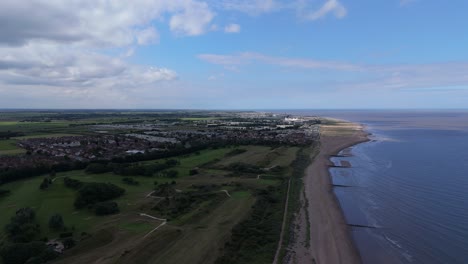 aerial view of a coastal town with a golf course, beach, and sea under a cloudy sky