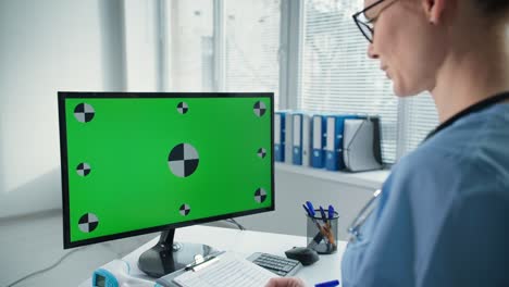 doctora médica trabaja en su computadora personal con una gran pantalla verde, el clínico consulta al paciente en línea mientras está sentado en el lugar de trabajo en el hospital