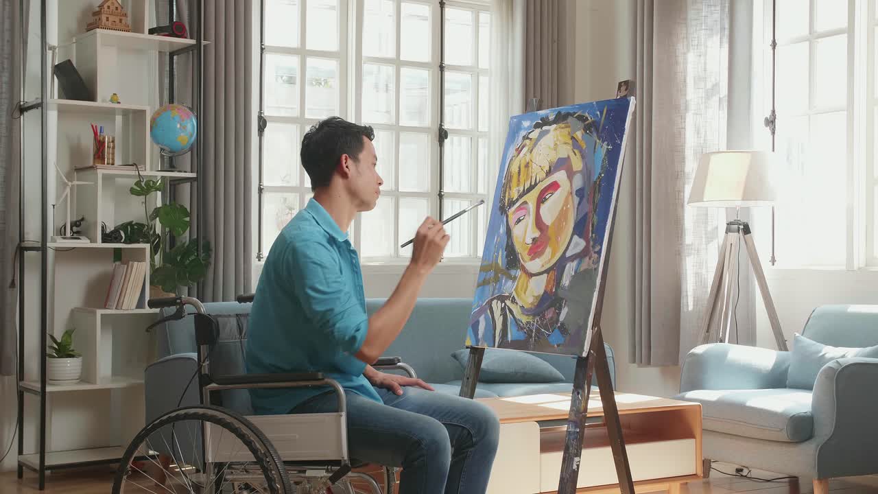 Side View Of An Asian Artist Man In Wheelchair Holding Paintbrush Mixed Colour Thinking And Painting A Girl On The Canvas
