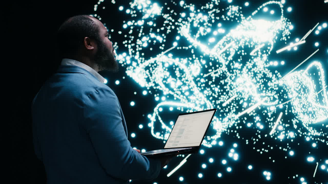 Man Using Laptop with Abstract Data Visualization on Large Screen