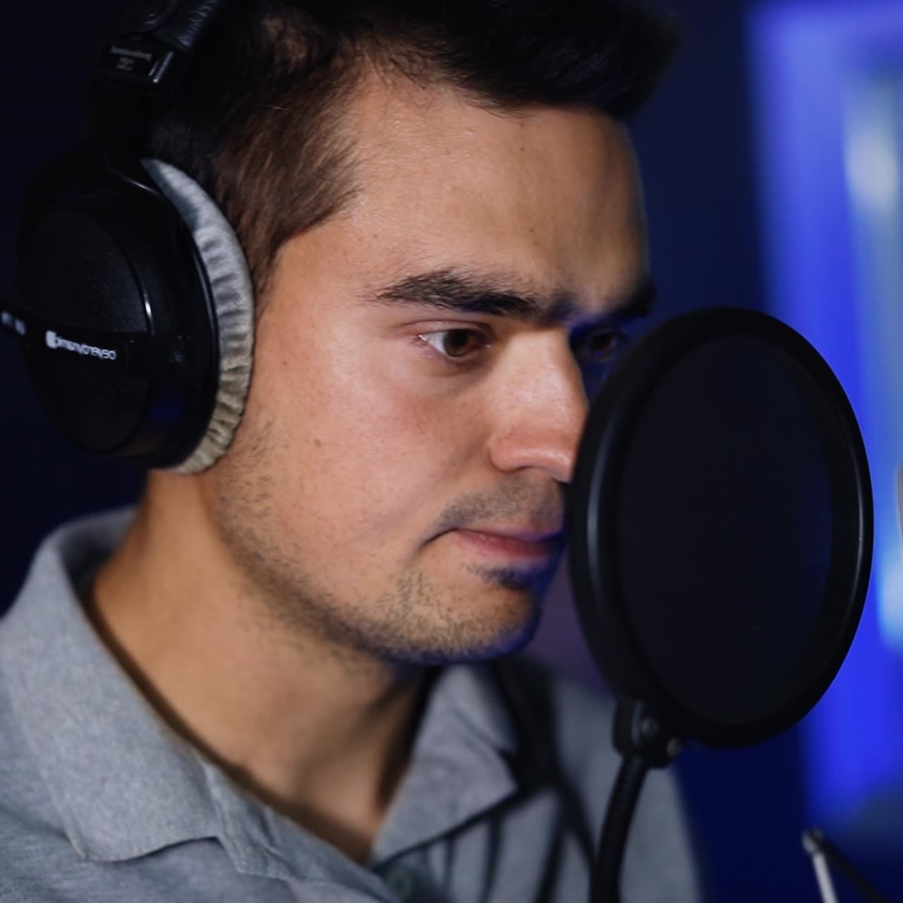 Uomo caucasico in piedi davanti al microfono professionale in attesa dell'inizio della canzone. Il cantante con le cuffie ascolta la musica in studio.